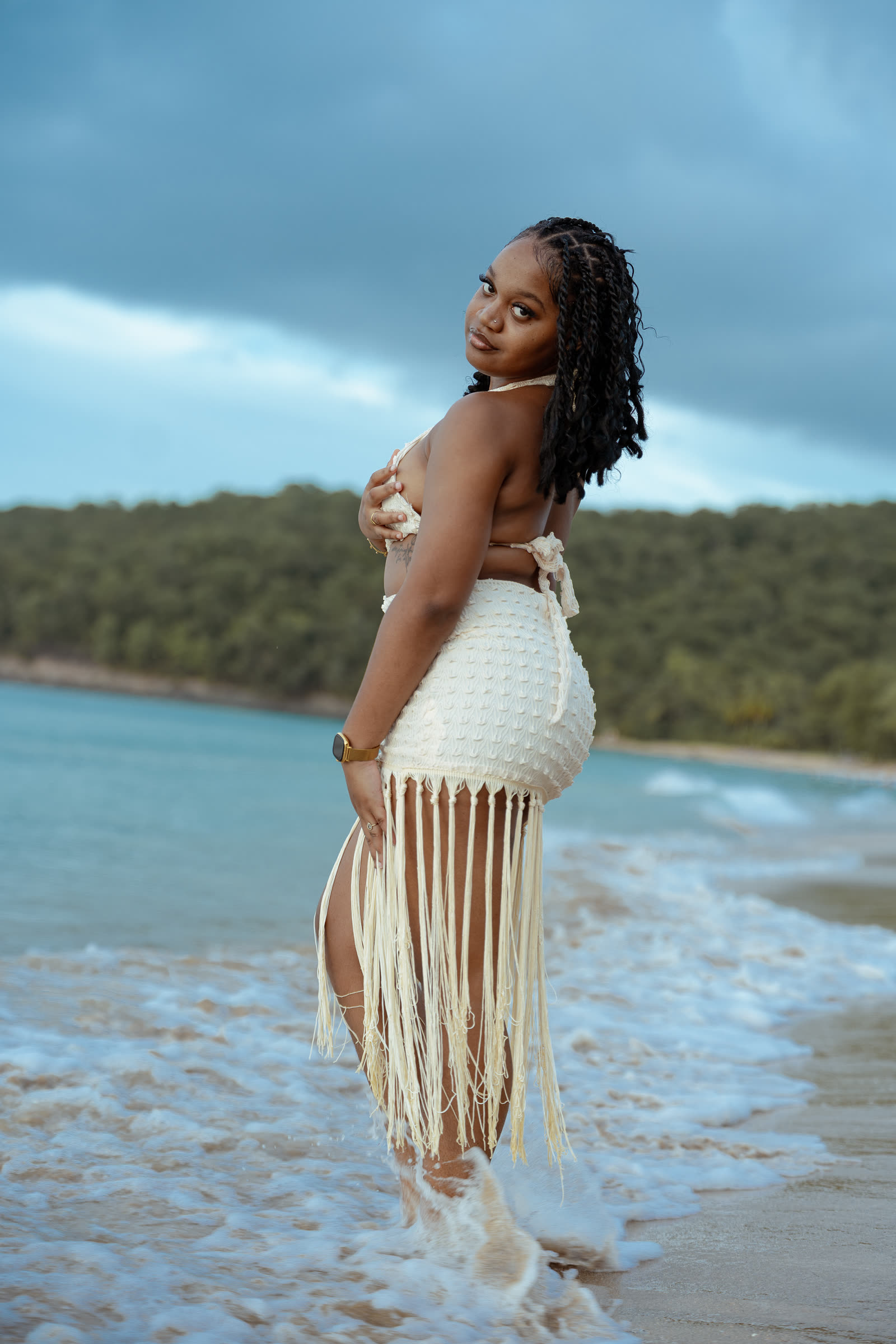 Loana de dos dans les vagues, le regard par-dessus l'épaule, la côte verte au loin